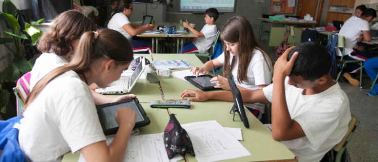 Varios alumnos en un aula utilizando dipositivos electrónicos como ordenadores y tabletas.