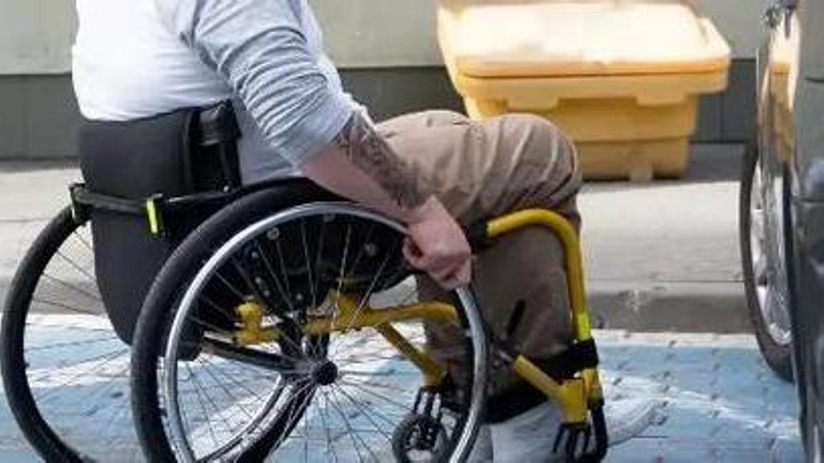Una persona en silla de ruedas se dispone a subir a un vehíuclo en una plaza reservada.