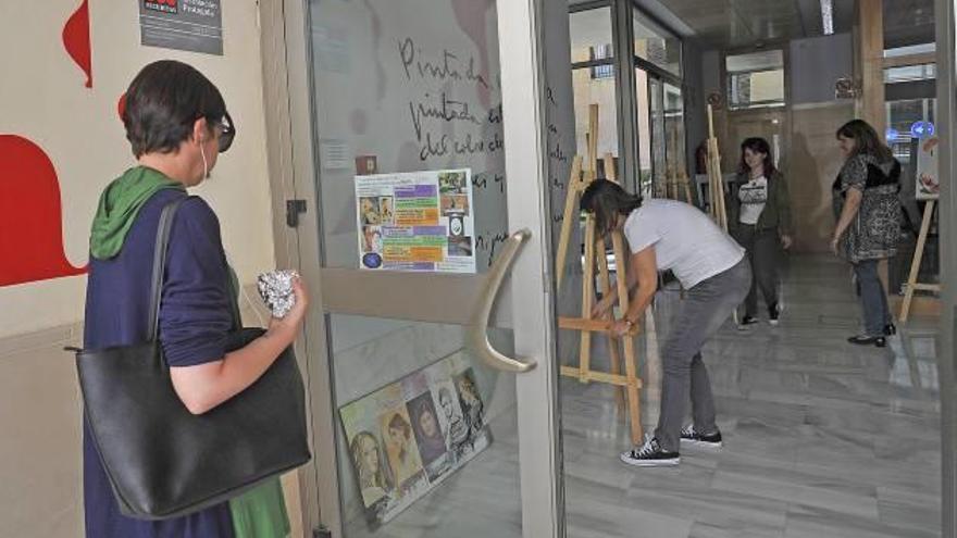 Una mujer observa el cartel con las actividades de la Asociación de Bellas Artes, mientras dentro se monta una exposición.