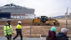 Operarios y turistas se mezclan en el Moll Adossat del Port de Barcelona, en obras, con las grúas de la terminal APM de fondo.