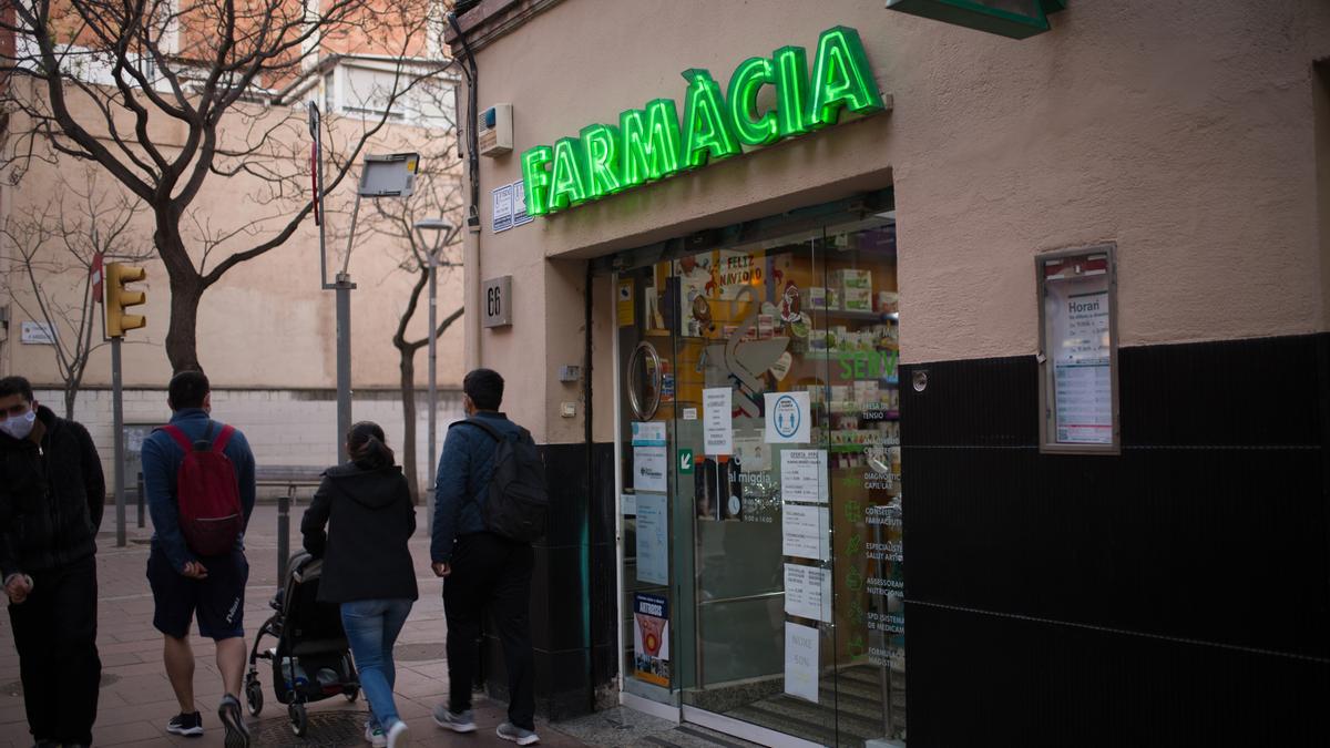 Varias personas pasan al lado de una farmacia.