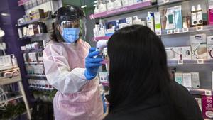 Una farmacéutica toma la temperatura a una mujer antes de realizarle un test de antígenos en la Farmacia Las Gemelas en Madrid.