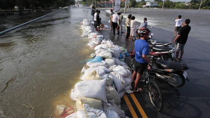 Varias personas, junto a un precario dique de contención en una calle anegada en Tailandia.