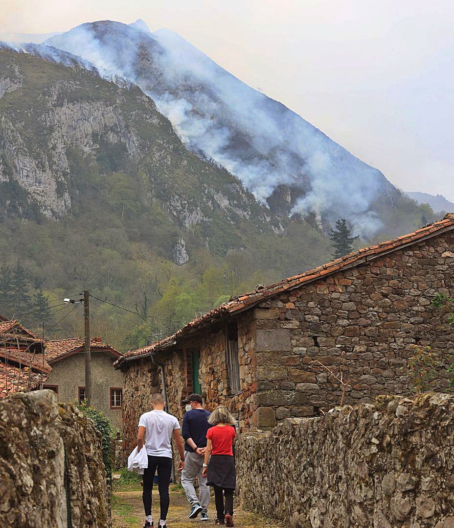 Paseantes por el pueblo de El Pedroso, con el humo del incendio al fondo