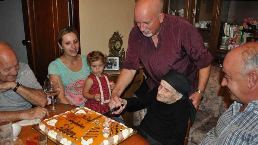 María Dolores Solino corta la tarta de su centenario con la ayuda de uno de sus hijos.