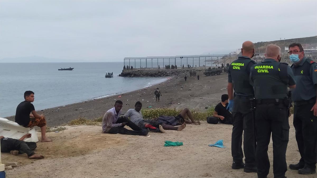 Miembros de la Guardia Civil conversan junto a un grupo de inmigrantes que han cruzado la frontera a nado