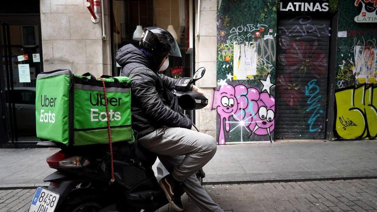 Un repartidor de UberEats espera un pedido en su motocicleta.