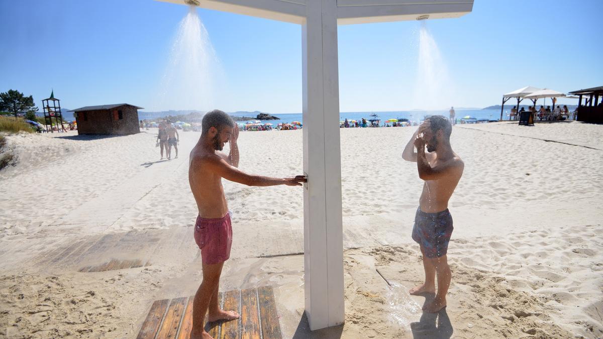Jóvenes refrescándose en las duchas de la playa de Areas en Sanxenxo.