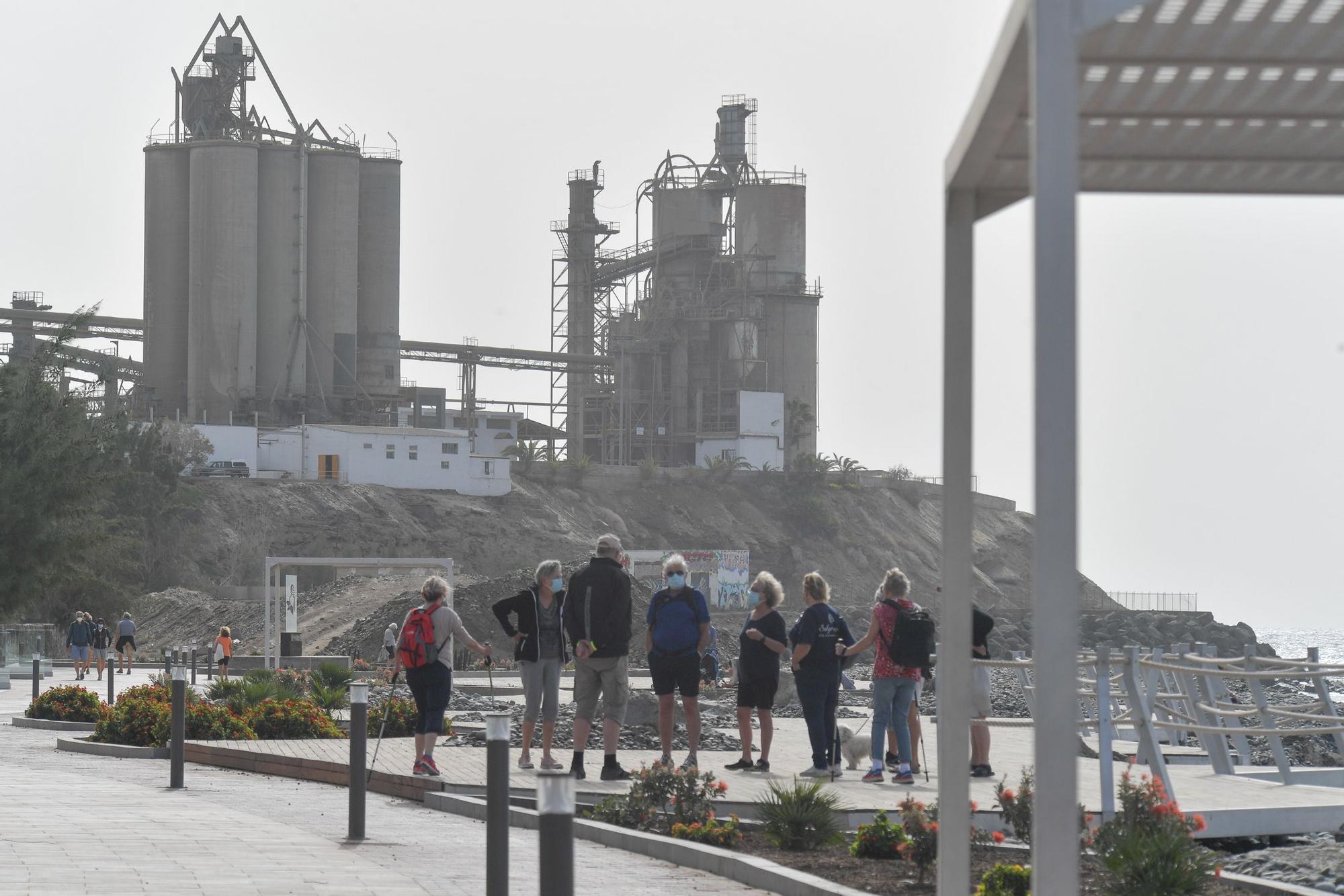 Un grupo de turistas visita el paseo marítimo de Santa Águeda con la cementera de fondo.