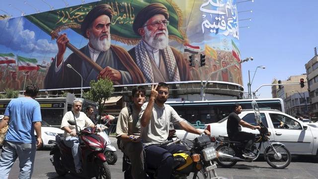 Un motorista iranià fa el senyal de la victòria mentre passa per davant d’un cartell dels aiatol·làs morts Khomeini i Khamenei, a Teheran. | ABEDIN TAHERKENAREH / EFE