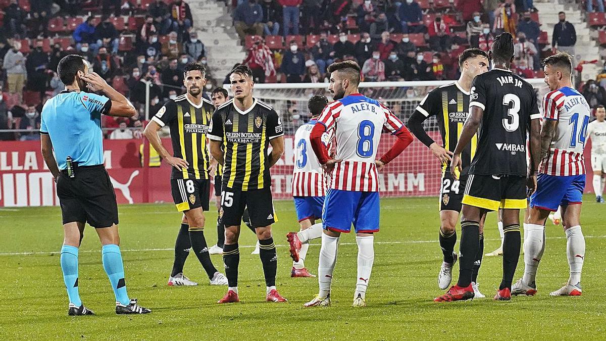 L’àrbitre escoltant el VAR i els jugadors esperant abans que invalidés el gol d’Aleix Garcia. | MARC MARTÍ