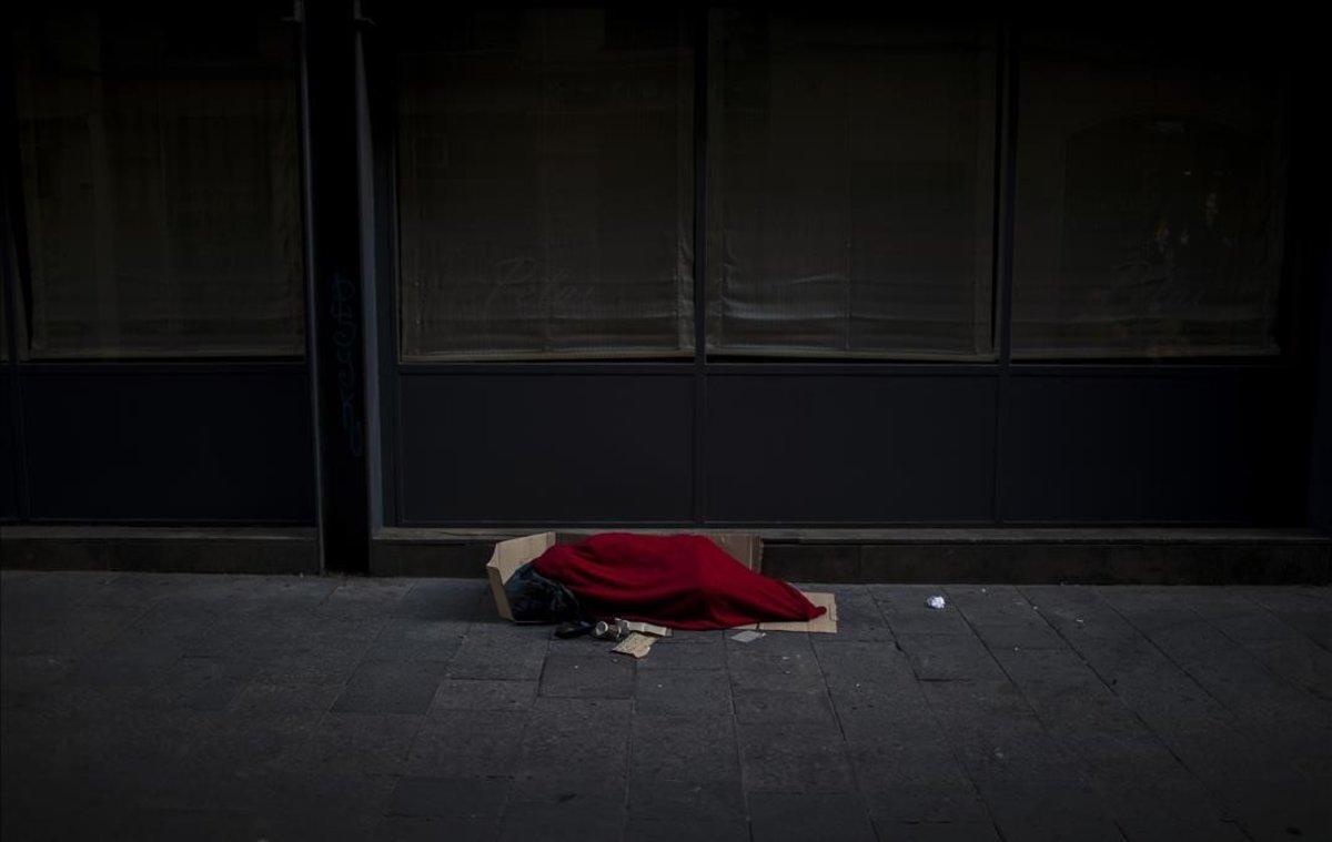 Un hombre cubierto con una manta en una calle vacía.