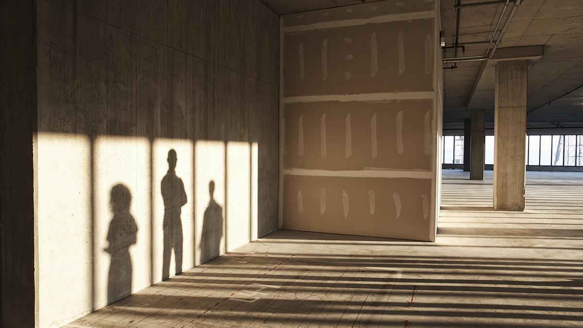 Shadows of business people cast on the sheet rock wall of a large empty raw office space.