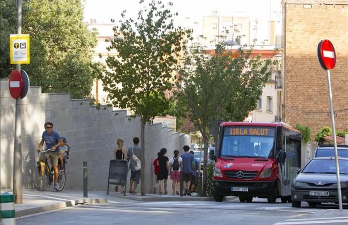 Unos turistas pasan a pie junto al autobús de la línea 116 en su camino hacia el parque Güell.