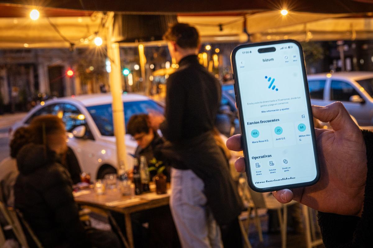 Una persona utilizando Bizum en un restaurante para pagar su parte de la cuenta conjunta. Desde junio, podrá pagar directamente la cuenta con su móvil y sin necesidad de tarjeta física, gracias a Bizum Pay