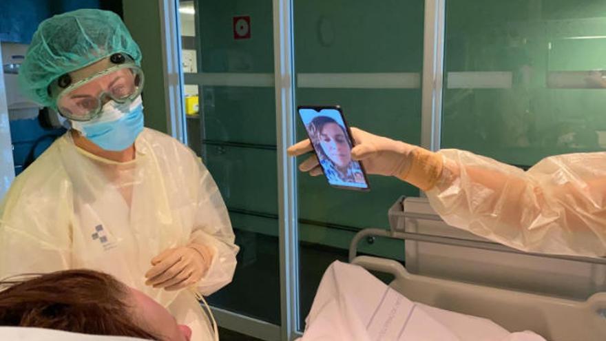Un sanitario sujeta un móvil para que un paciente pueda comunicarse con su familia a través de videollamada.