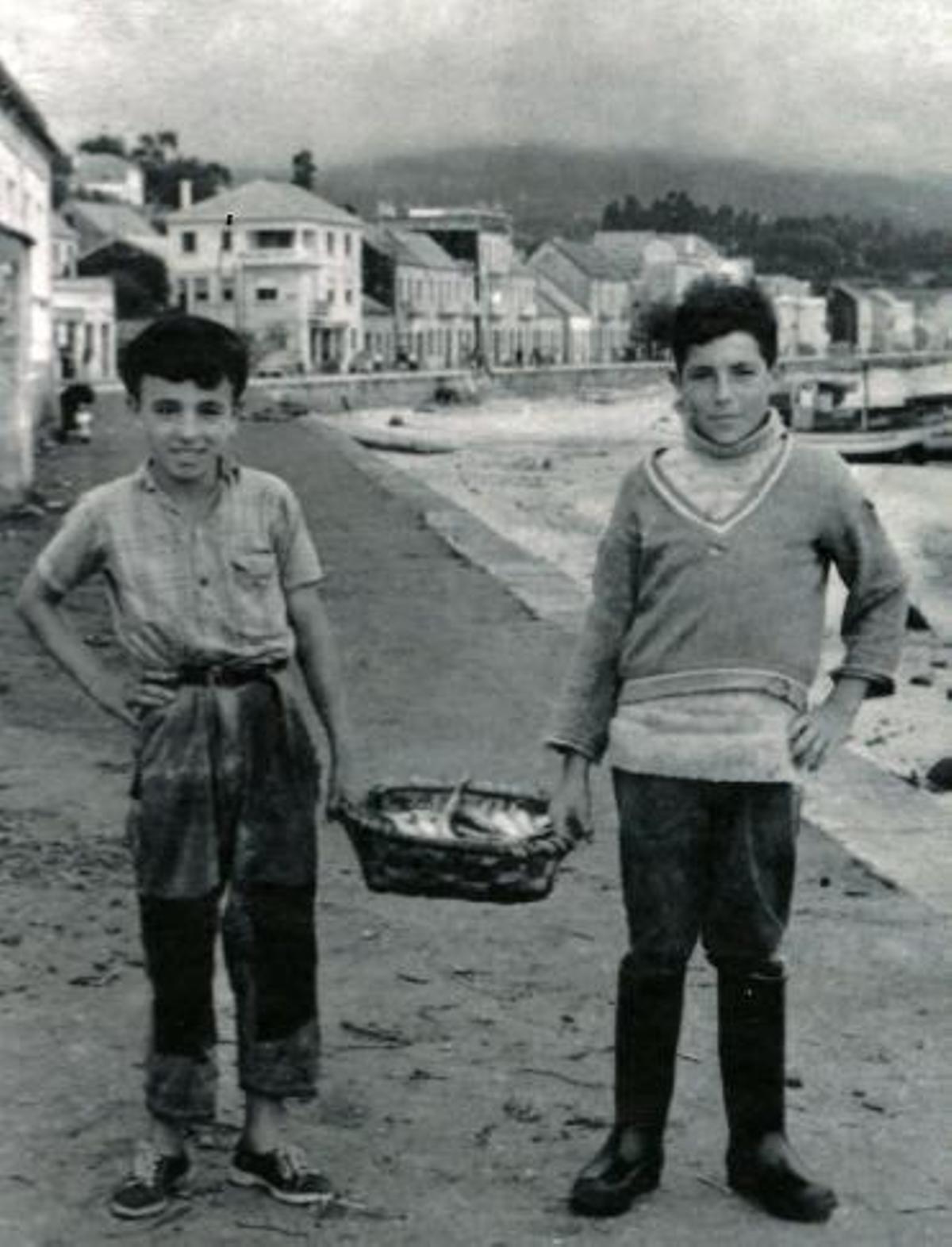 Dous rapaces de a bordo dun barco da ardora, cunha patela chea de sardiñas.