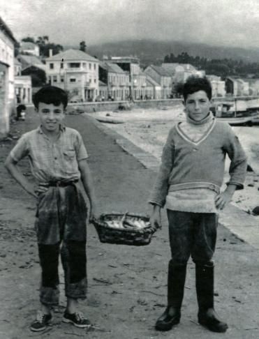 Dous rapaces de a bordo dun barco da ardora, cunha patela chea de sardiñas.  