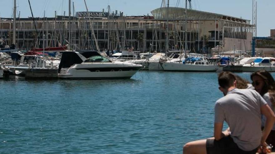 Un grupo de jóvenes toma el sol en el muelle Pedro Herrero del Puerto de Alicante, propietario del centro de ocio Panoramis, que se observa al fondo.