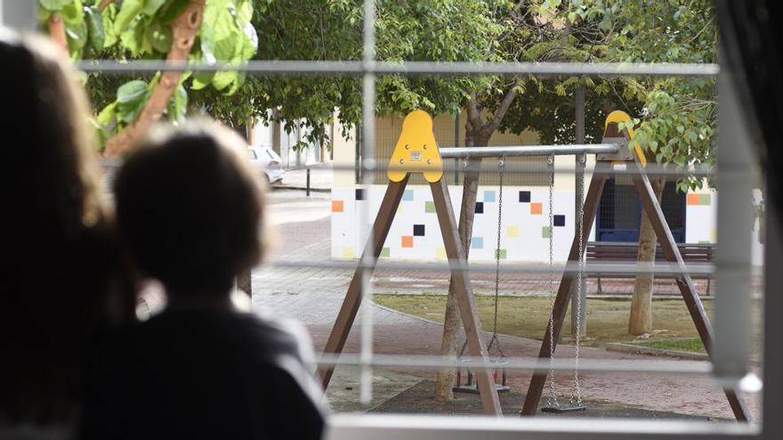 Unos niños miran por la ventana un parque infantil, cerrado.