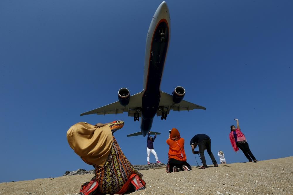 Turistas hacen fotos a los aviones que pasan por encima de la playa tailandesa de Mai Khao.