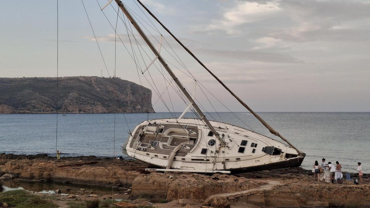 El velero encallado y, a la izquierda, un grupo de turistas despliega sillas y mesas para cenar a la orilla del mar