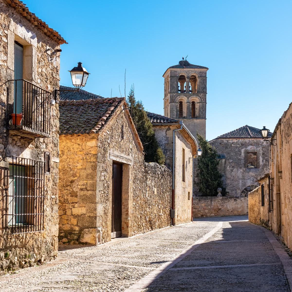 Calle de hermosos edificios medievales con torre de iglesia al fondo en la ciudad monumental de Pedraza, Segovia.