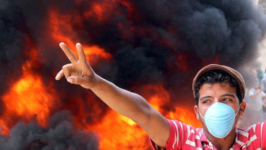 Un jove fa el signe de la victòria a la plaça Tahrir del Caire plena de flames i fum.