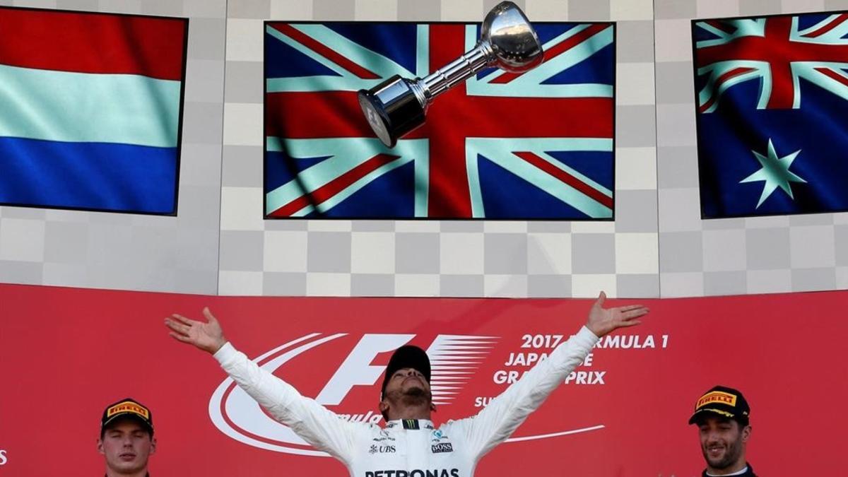 Lewis Hamilton lanza el trofeo de ganador del GP de Japón al aire ante la mirada de Max Verstappen, a la izquierda, y Daniel Ricciardo.