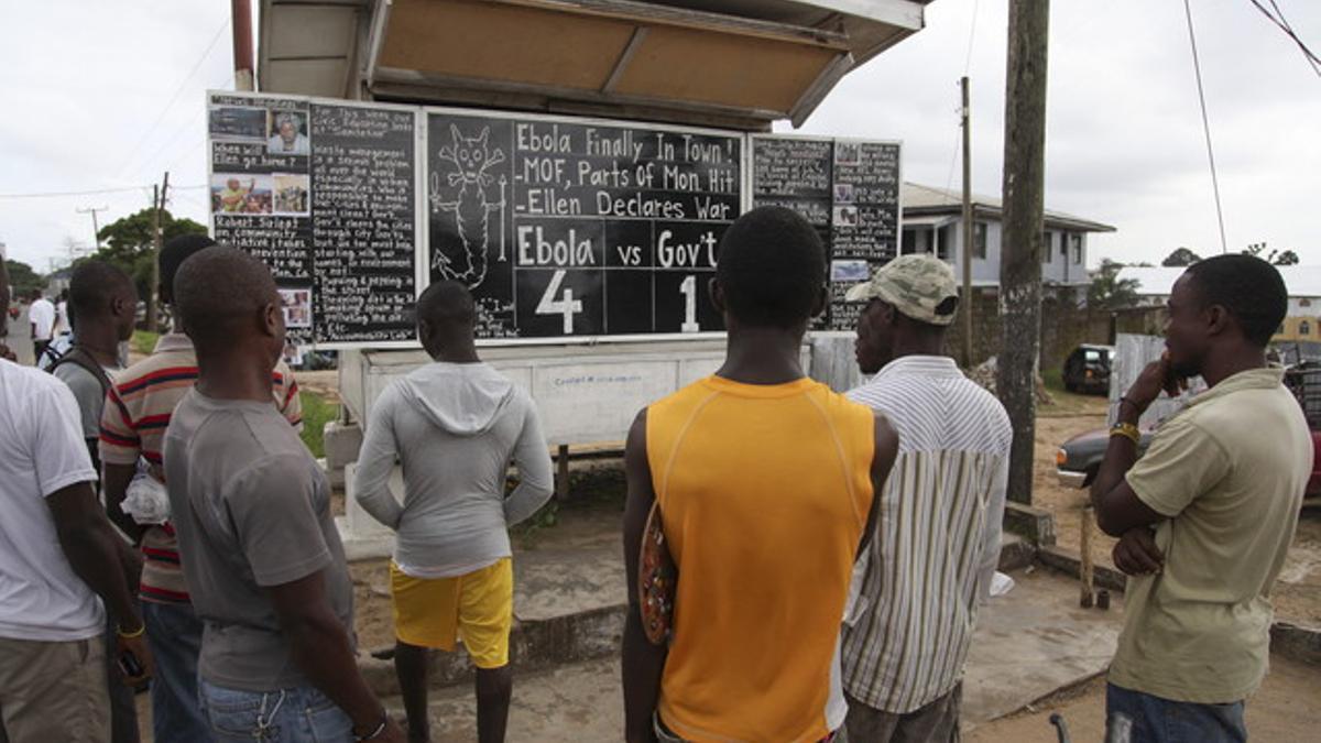Varios vecinos de Johnsville, cerca de Monrovia (Liberia), observan el tablero que anuncia la cifra de víctimas mortales de ébola, el lunes.