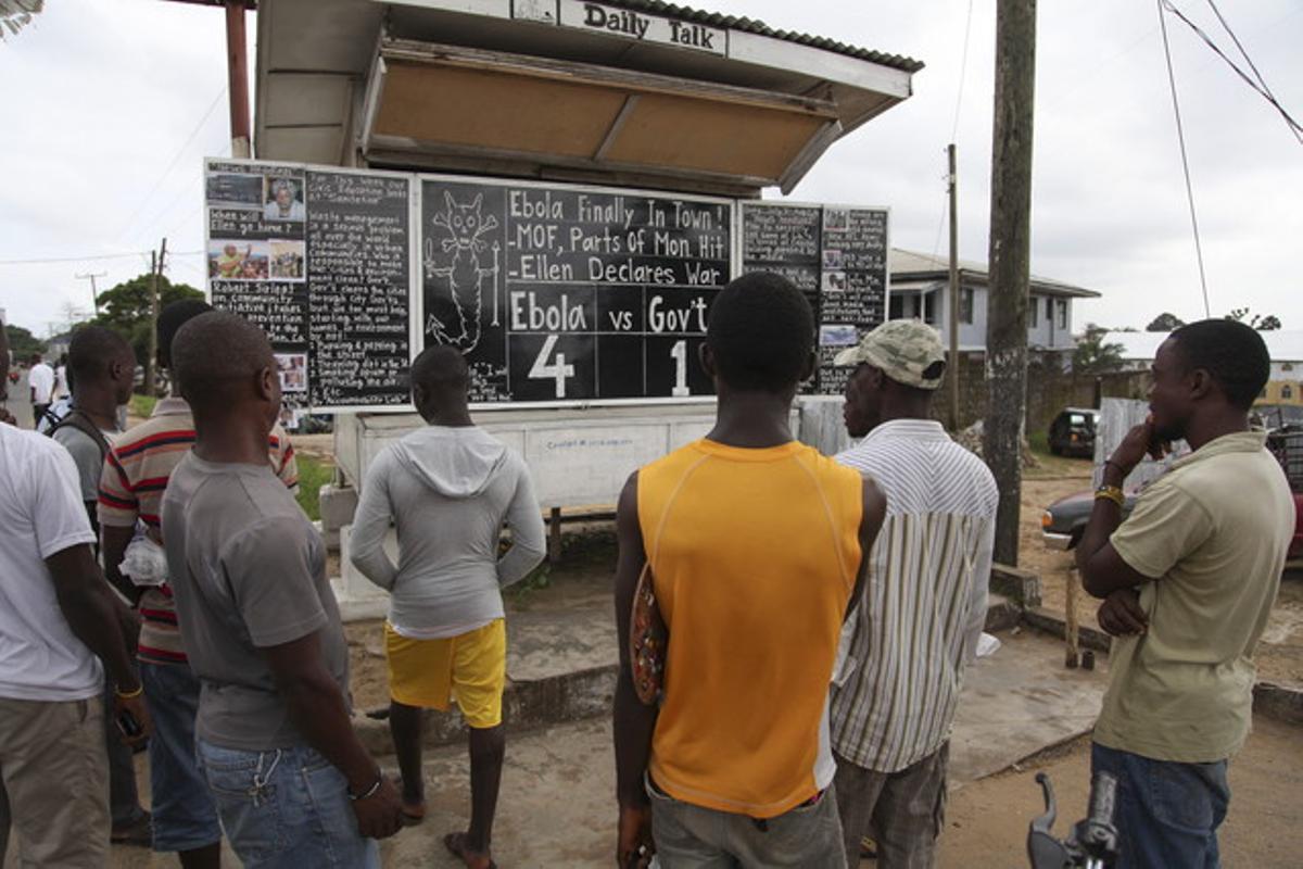 Diversos veïns de Johnsville, a prop de Monròvia (Libèria), observen el tauler que anuncia la xifra de víctimes mortals d’Ebola, aquest dilluns.
