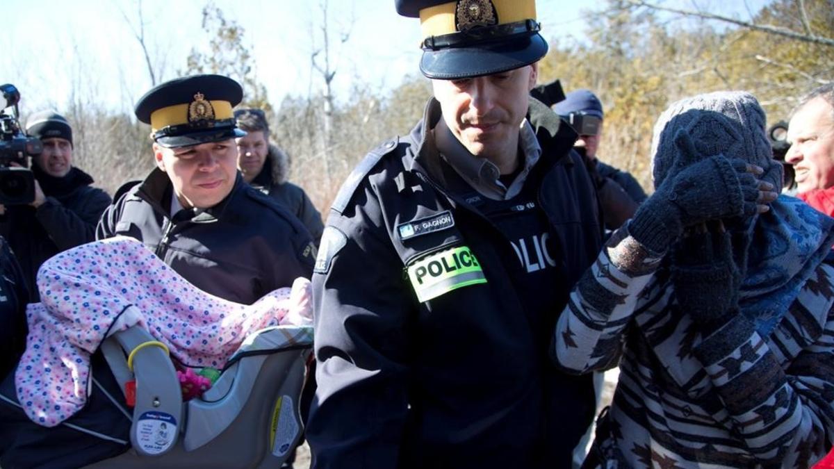 Una madre y su bebé escoltados por la policía montada de Canadá en la frontera con Quebec.