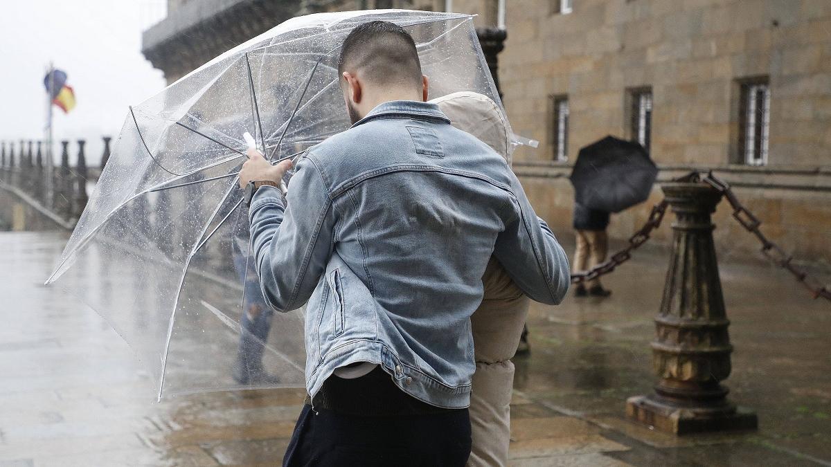 Una pareja de turistas intenta protegerse del viento y de la lluvia en el Obradorio