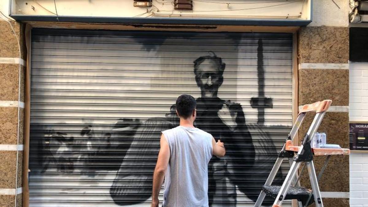 L'artista pintant un dels murals en una persiana.
