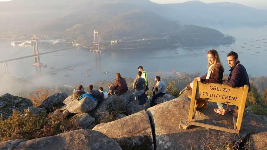 Unas personas contemplan la puesta de sol desde el banco de Cedeira, con la ría al fondo. // FdV