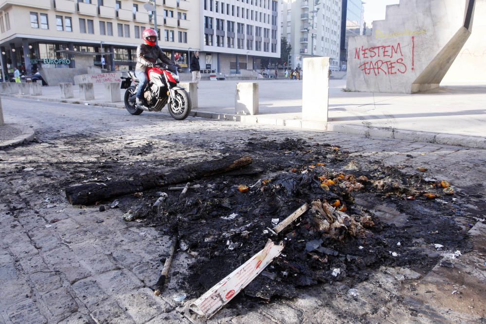 Carrers amb restes de mobiliari urbà cremat, contenidors per terra i treballadors de la brigada treballant