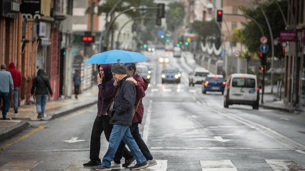 Varias personas cruzan un paso de peatones en Santa Cruz de Tenerife protegidos con paraguas.