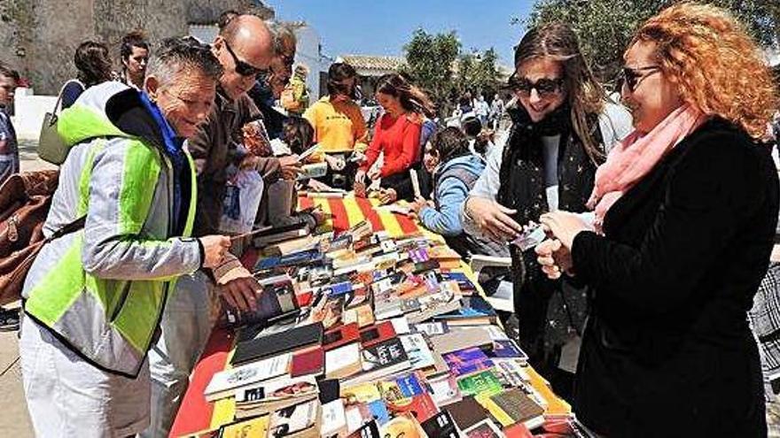 Vecinos y visitantes ante uno de los puestos de libros montado en la plaza de la Constitució por parte de la Biblioteca Marià Villangómez con motivo del día de Sant Jordi.