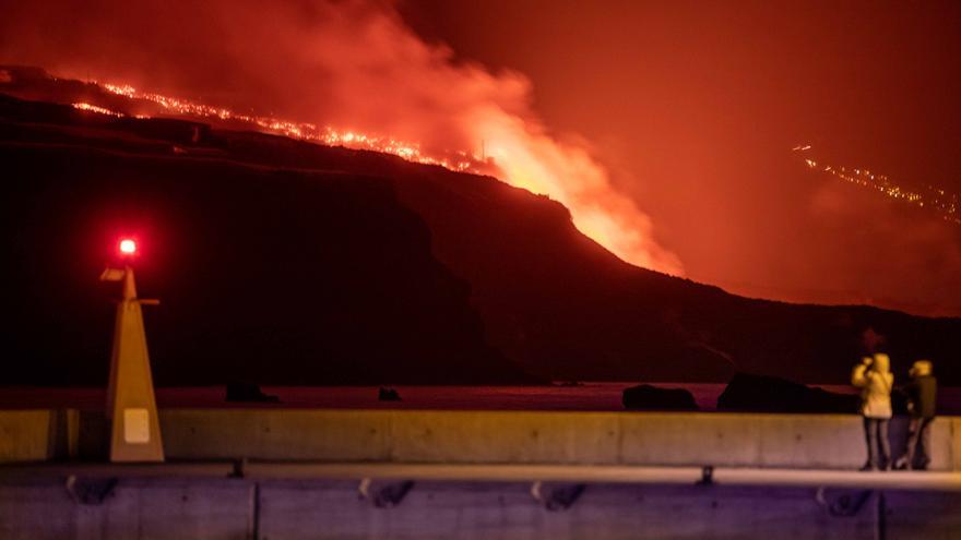 Varias personas observan la lava y piroclastos a su llegada a la playa de los Guirres