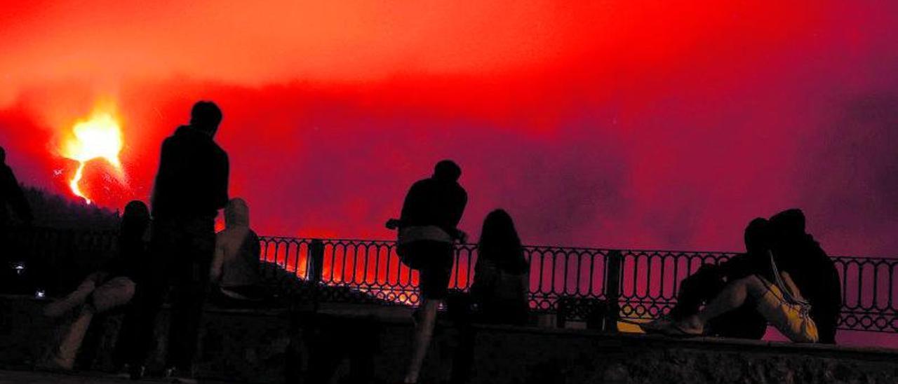 Varias personas observan  el cono volcánico la noche del pasado sábado desde la explanada de la iglesa de Tajuya, en El Paso.