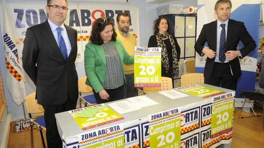 La presidenta de la asociación de comerciantes muestra el cartel del 20 aniversario.