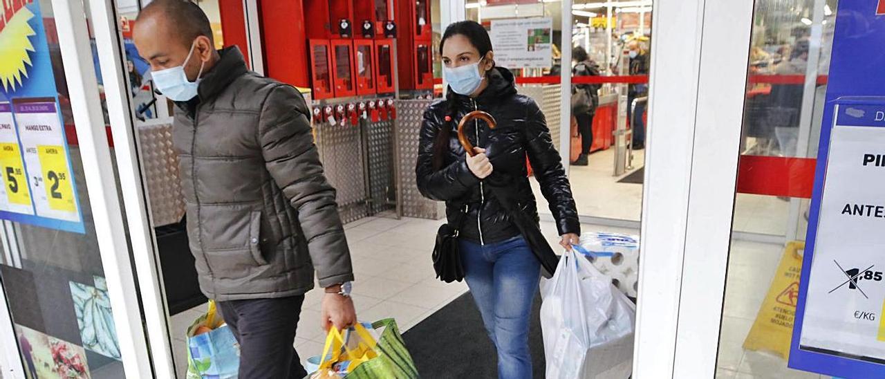 Dos personas salen con bolsas llenas de un supermercado de Travesía de Vigo. |   // ALBA VILLAR