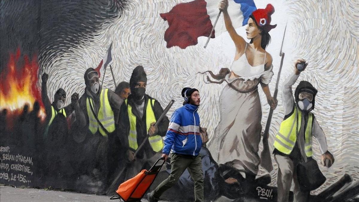 Un hombre pasa junto a un mural que reproduce una versión de 'La libertad guiando al pueblo', de  Eugene Delacroix, con la presencia de 'chalecos amarillos', idea del artista Pascal Boyart.