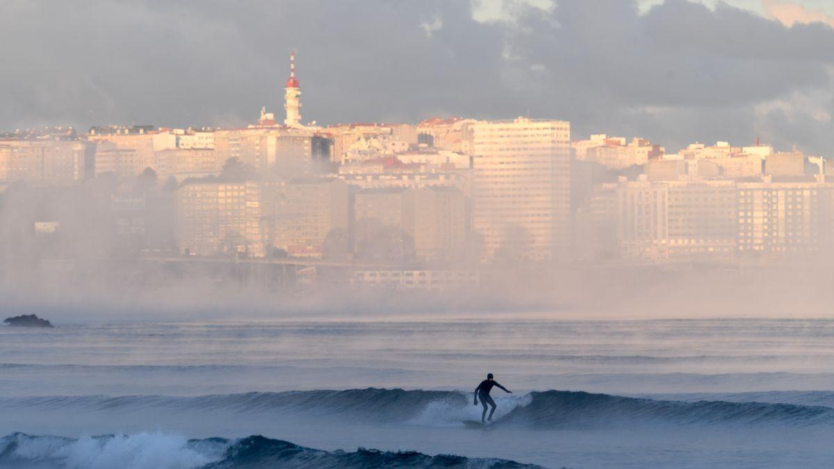 Un joven practicando surf con la ciudad de A Coruña al fondo.