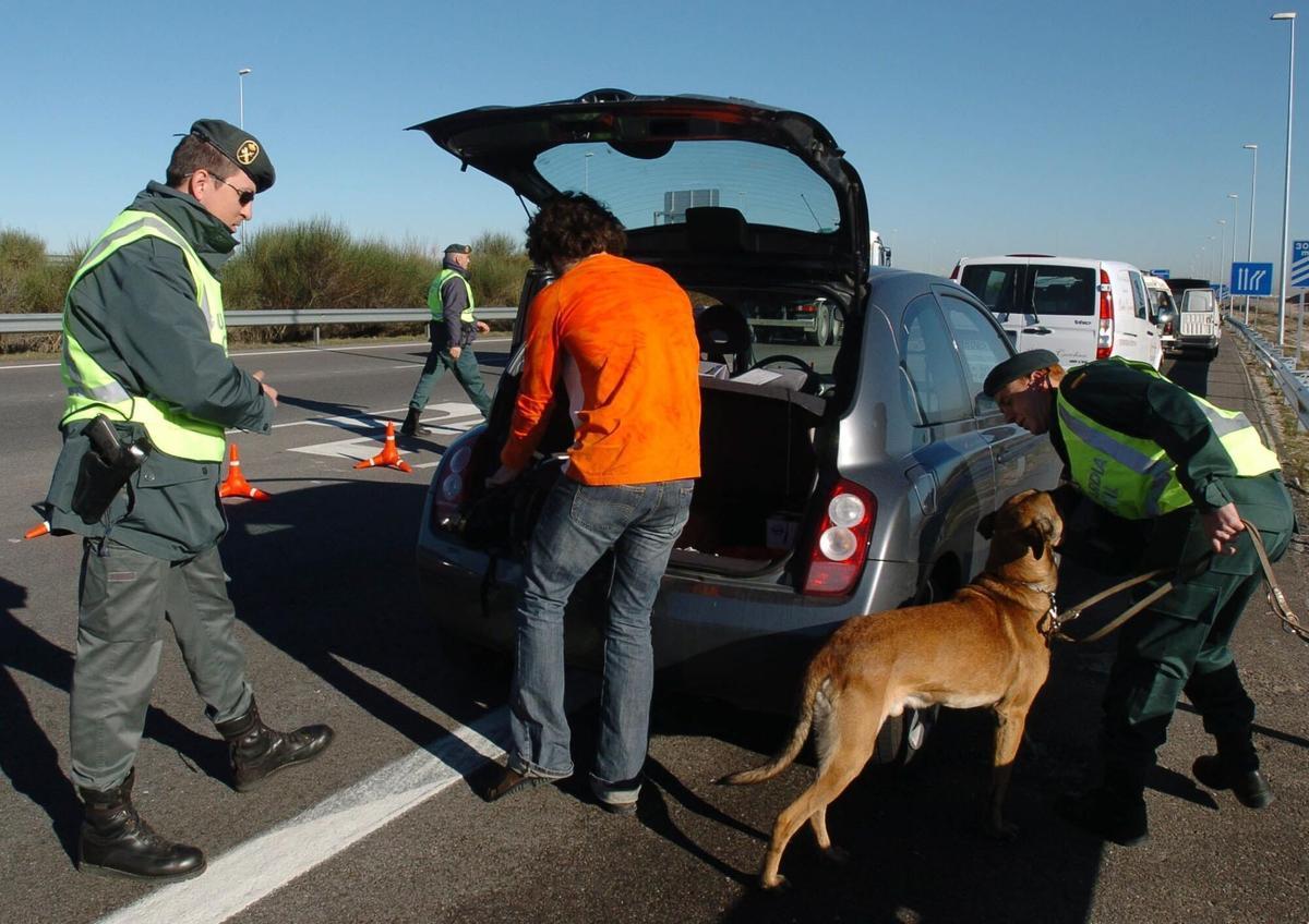 Agentes de la Guardia Civil ayudados de un perro registran el maletero de uno de los automóviles