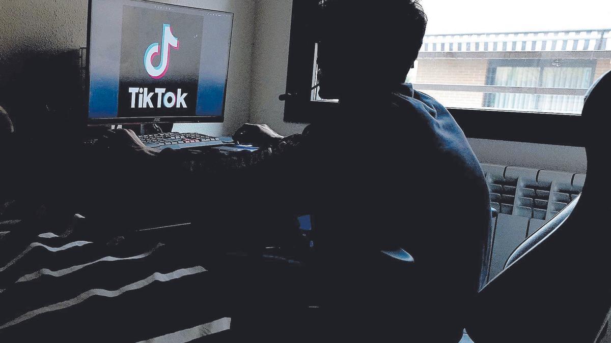 Un jove, enfront d'una pantalla amb el logotip de TikTok. Un adolescent mira l'aplicació Tik-*Tok