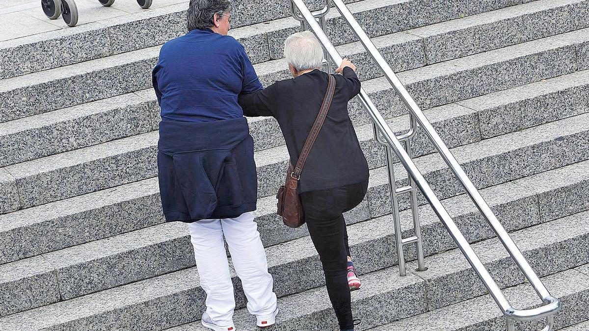 Una cuidadora ayuda a subir escaleras a una mujer dependiente en Santiago.