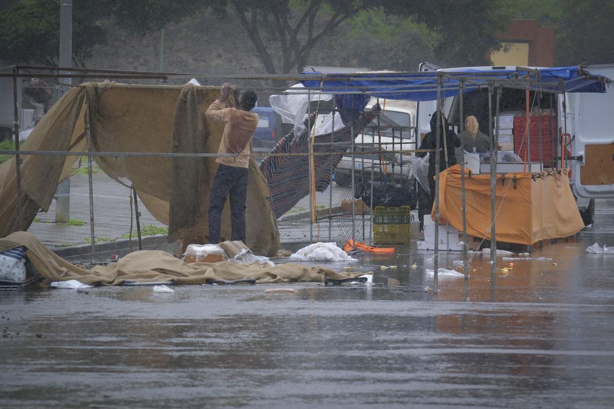 Vendedores de un mercadillo recogen sus puestos por la lluvia.