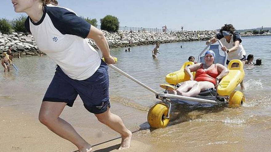 Dos monitoras transportan a una usuaria en una silla anfibia, ayer en la playa de Oza. / eduardo vicente