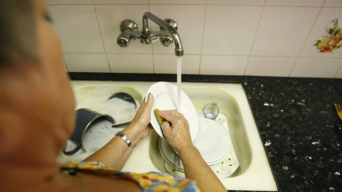 Una mujer lava los platos en su casa.